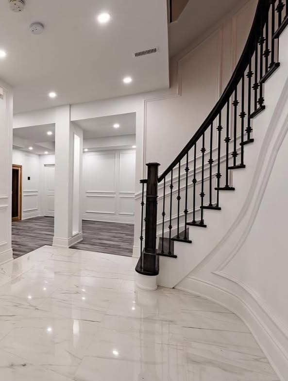 Interior with curved staircase, white paneled walls and polished floor tile.