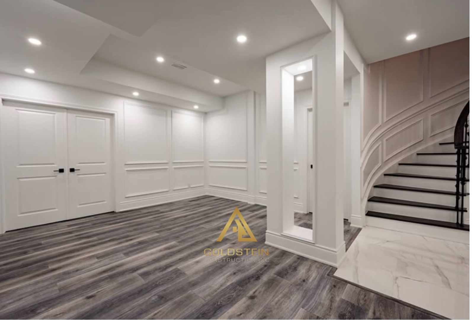Bright wainscoted lower level hallway with curved staircase and marble floor