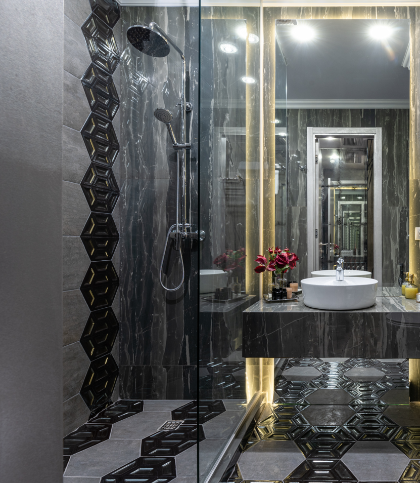 Luxury dark bathroom with glass shower enclosure and geometric floor tile.