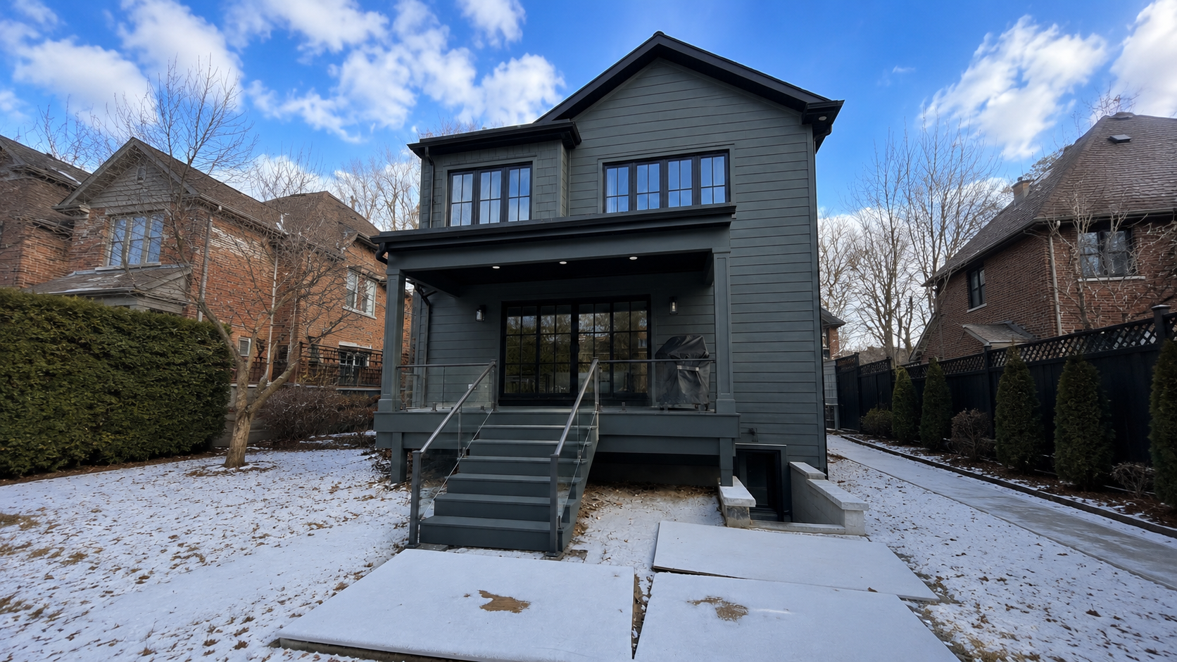 Modern custom home exterior featuring dark contemporary siding, large black-framed windows, and a sleek rear patio deck with glass railings