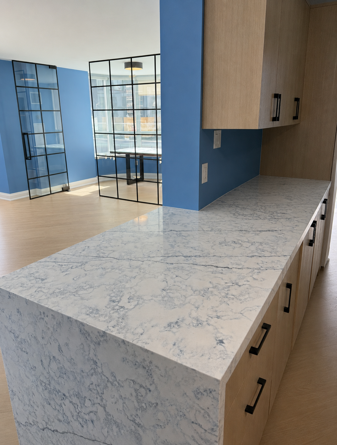 Empty condo interior with marble waterfall island and steel-framed glass doors — mid interior remodel in Richmond Hill